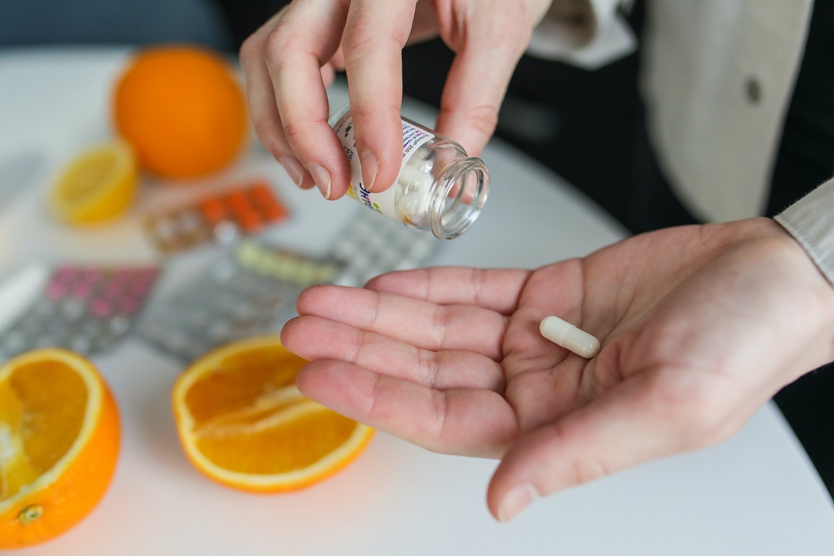 picture of person taking a pill standing beside a table with pills and orance on it