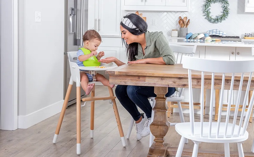 picture of a toddler sitting in a high chair in the kitchen beside woman who is sitting next to the dining table