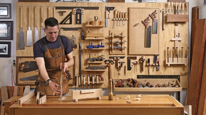 a person woodworking with a lot of hand tools behind him